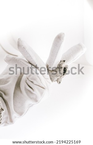 Hands in white gloves presented white gold panthere ring in diamonds and emeralds on a white background