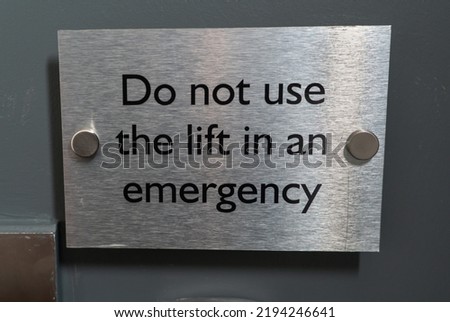"Do not use the lift in an emergency" sign next to the elevator door. Safety rules during the evacuation. Fire regulations for safety of the people. Gray metal sign in English.