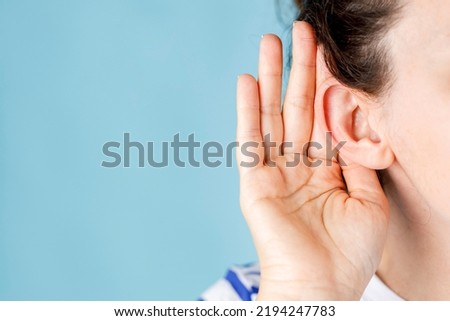 Young woman who has trouble hearing what the other person is saying. Hand is holding ear of woman to hear better  Royalty-Free Stock Photo #2194247783
