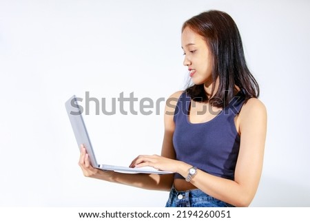 Portrait isolated studio cutout shot of Asian female model smiling look at camera holding pointing green blank screen laptop computer showing product promotion advertisement on white background.