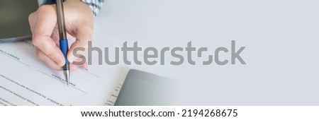 Close-up of hand with a pen on the background of paper official documents. Employment contract signature. Employee in a check shirt signs a hiring document. Banner with free space for text