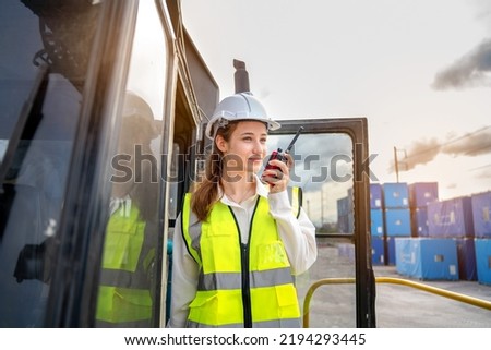 Female Foreman stay on lifting forklift container cargo forklift using walkie talkie for communication and control forklift concept service transportation logistic. Safety supervisor in white helmet Royalty-Free Stock Photo #2194293445