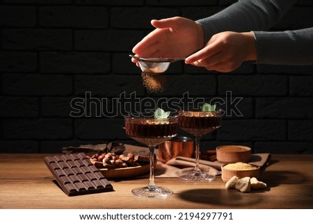 Woman decorating hot chocolate with cocoa powder at wooden table, closeup