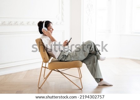 Uses the audio player app listens to music with headphones break relaxation. A woman is resting on a sofa in an apartment