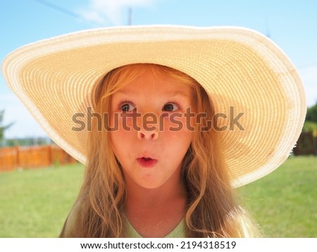 little cute naughty girl with a big straw hat looks surprised and funny on a beautiful summer sunny day