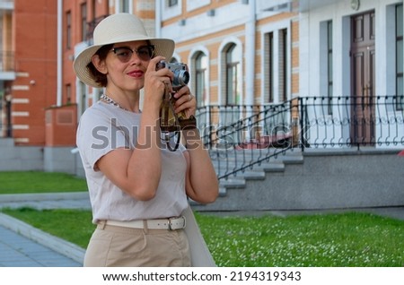 Blue color toned photo of beautiful woman tourist in a straw hat takes pictures on the street with a vintage camera