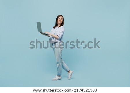 Full body side view young happy smiling woman she 20s wears casual blouse hold use work on laptop pc computer look aside isolated on pastel plain light blue background studio People lifestyle concept