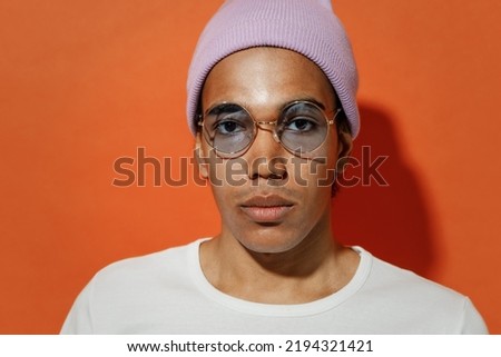 Close up cropped frowning upsed unnerved stupefied young black curly man 20s years old wears white t-shirt pink hat glasses looking camera isolated on plain pastel orange background studio portrait Royalty-Free Stock Photo #2194321421