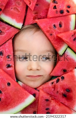 The face of a child in a frame of watermelon slices.Red berry pulp.A boy framed by triangular pieces of watermelon.Funny summer picture.Cute portrait of a baby.Child with watermelon