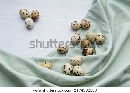 Fresh little quail eggs on white wooden background with space for text Easter banner, pastel green napkin  textile top view