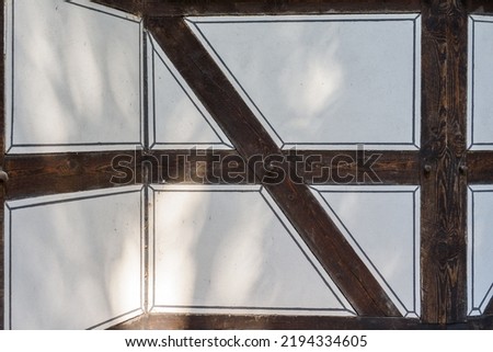 Detail of an old half-timbered made of dark brown wooden beams and white plastered spaces with painted decor. Half-timbered detail of a model building house in dark brown and white. Half-timbered.  Royalty-Free Stock Photo #2194334605