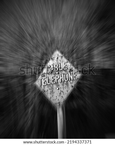 Black and white metal sign on a post. Rusty, weathered, aged and unique. Stating "Cable Telephone", in a heavy bold metal font. Vignette and motion blur added giving a startling effect.