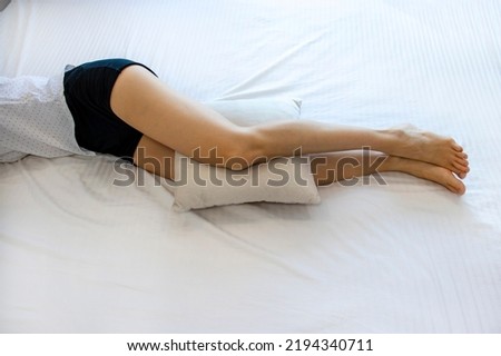 A woman with an anatomical pillow between her legs and knees, lying on a bed with white sheets. A girl resting on her side Royalty-Free Stock Photo #2194340711