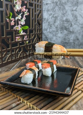 chopstick holding Sushi with shrimps, prawn on a black plate with dark background