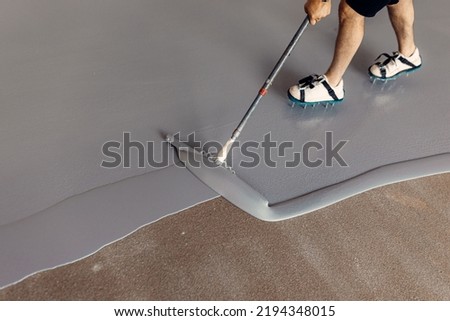A construction worker applying grey epoxy resin in an industrial hall Royalty-Free Stock Photo #2194348015
