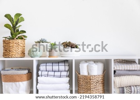 Potted plants in ecology straw baskets on shelf of bed linens cupboard textile arrangement storage organization. Minimalism Scandi placed method neatly folded cotton fabric bedding material copy space Royalty-Free Stock Photo #2194358791