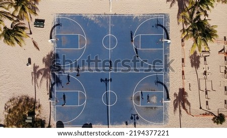 An aerial top view of people playing on blue basketball courts on a sandy beach surrounded by palm trees