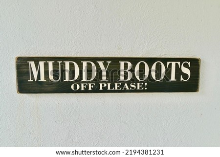 A closeup of a Muddy Boots Off Please sign on a white wall