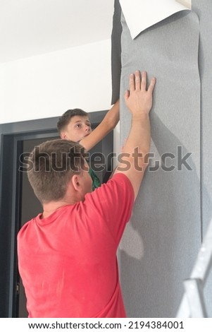A man glues vinyl wallpaper on the wall, repair in the room and wallpapering, gray wallpaper. Royalty-Free Stock Photo #2194384001