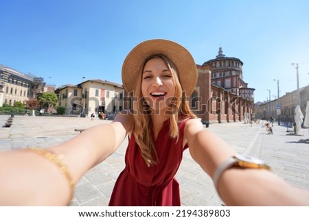 Smiling tourist takes selfie with the church of Santa Maria delle Grazie which preserves "The Last Supper" by Leonardo da Vinci, Milan, Italy
