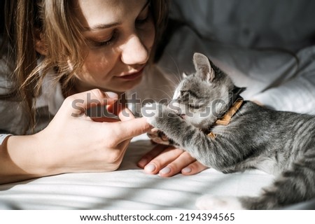 Candid portrait of Young woman is resting with kitten on the bed at home one sunny day. Girl play with outbred kitten. Royalty-Free Stock Photo #2194394565