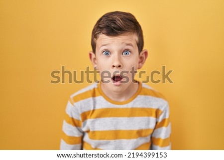 Young caucasian kid standing over yellow background afraid and shocked with surprise expression, fear and excited face. 