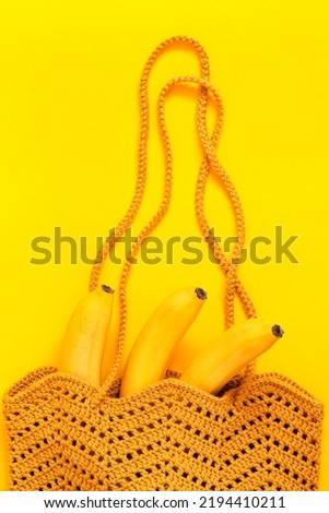 Bright orange crochet bag with bananas on a yellow background. Eco friendly shopping and healthy lifestyle concept. Top view. Copy space.