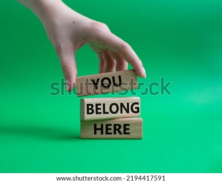 You belong here symbol. Wooden blocks with words You belong here. Beautiful green background. Businessman hand. Business and You belong here setbacks concept. Copy space.