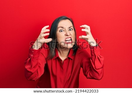 Middle age hispanic woman wearing casual clothes shouting frustrated with rage, hands trying to strangle, yelling mad  Royalty-Free Stock Photo #2194422033