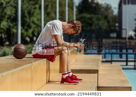 side view of tired sportsman sitting with sports bottle near ball