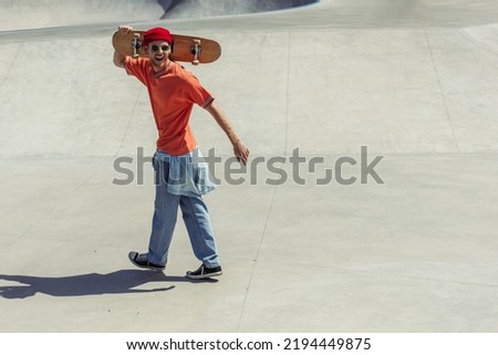 full length of man in jeans and sunglasses walking with skateboard in skate park