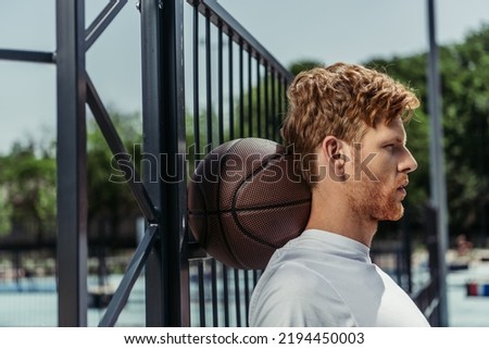 side view of redhead sportsman standing with ball near fence