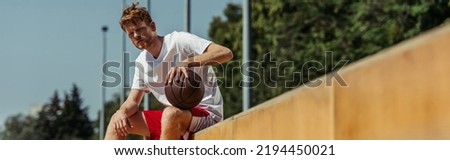 redhead basketball player sitting on stadium with ball, banner