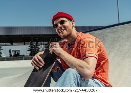 happy man in stylish outfit sitting with skateboard outdoors
