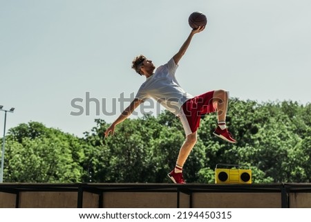side view of man in sportswear playing basketball near record player