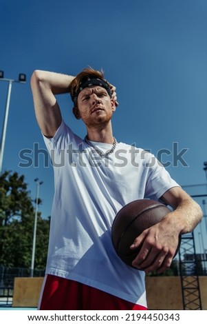 low angle view of basketball player in white t-shirt and necklace holding ball outdoors
