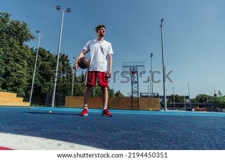 full length of basketball player in sportswear standing with ball on modern court