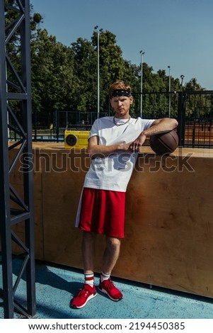 full length of basketball player in red shorts standing near boombox and looking at camera