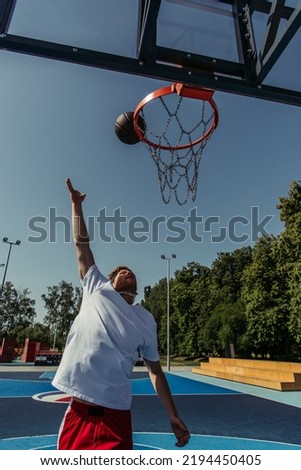 man in white t-shirt throwing ball into basketball hoop on court