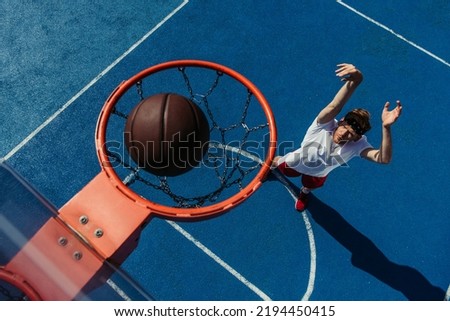 top view of ball in basketball ring and young man training on court