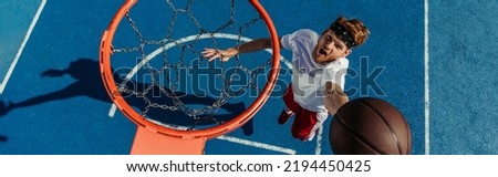 top view of young thrilled man throwing ball into basketball hoop, banner