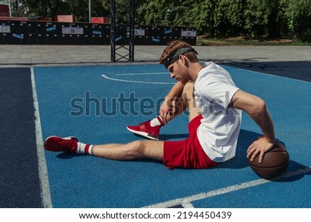 basketball player in red shorts and sneakers sitting on court near ball