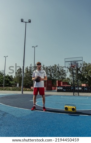 full length of sportive man with ball standing on basketball court near boombox