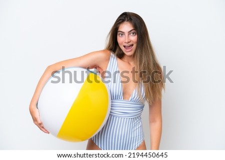 Young woman in swimsuit holding beach ball isolated on white background with surprise and shocked facial expression