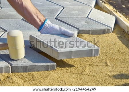 A builder with a hammer in his hands lays paving slabs in the garden