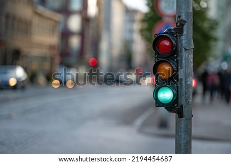 blurred view of city traffic with traffic lights, in the foreground a semaphore with a green light Royalty-Free Stock Photo #2194454687