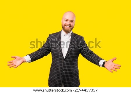 Picture of a bearded businessman smiling at the camera while he wants a hug over yellow wall .