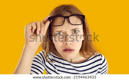 Confused woman looks at you with suspicious, doubtful and incredulous expression on her face. Close up of skeptical and suspicious young woman looking out from under glasses on orange background. Royalty-Free Stock Photo #2194463433