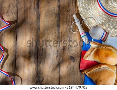 Chilean independence day concept. fiestas patrias. Tipical baked empanadas, wine or chicha, fat and play emboque. Decoration for 18 september party day, wooden background, top view. Royalty-Free Stock Photo #2194479705