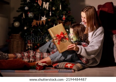 young mother and daughter open Christmas Lighting Present Gift Box front of Xmas Tree. Happy Mom with kid girl in Magic Night. Family merry christmas and new year holiday concept. High quality photo.